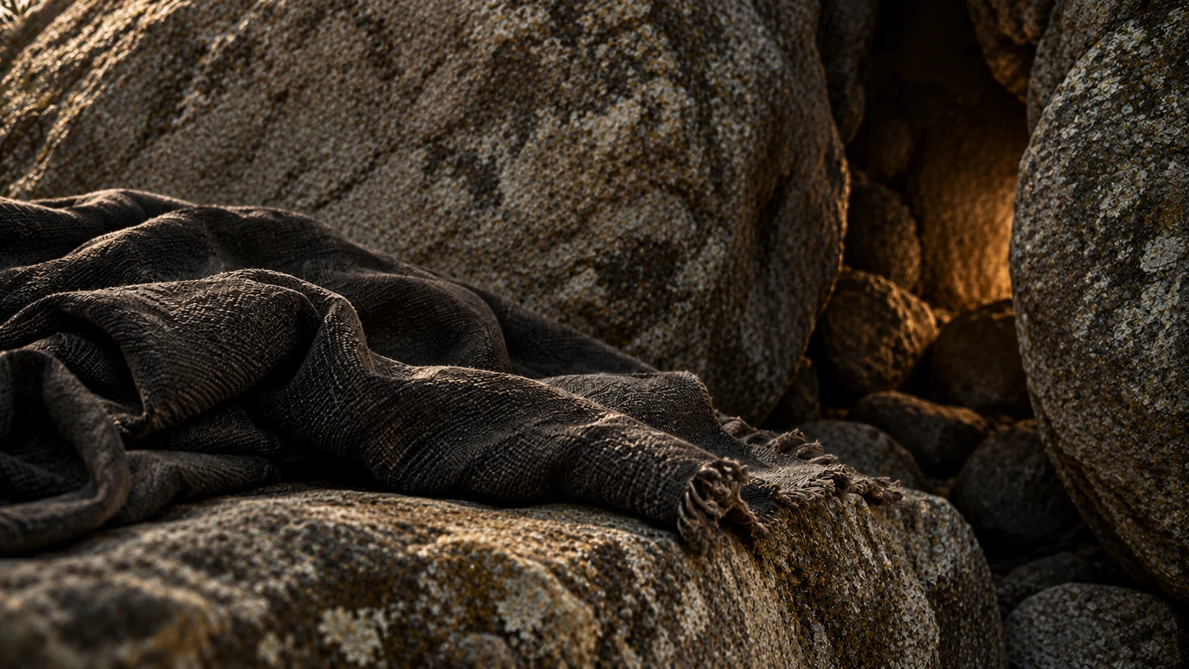 Visibly empty flat dark fabric folds rest on irregular natural stone beside a narrow warm-shadow gap.