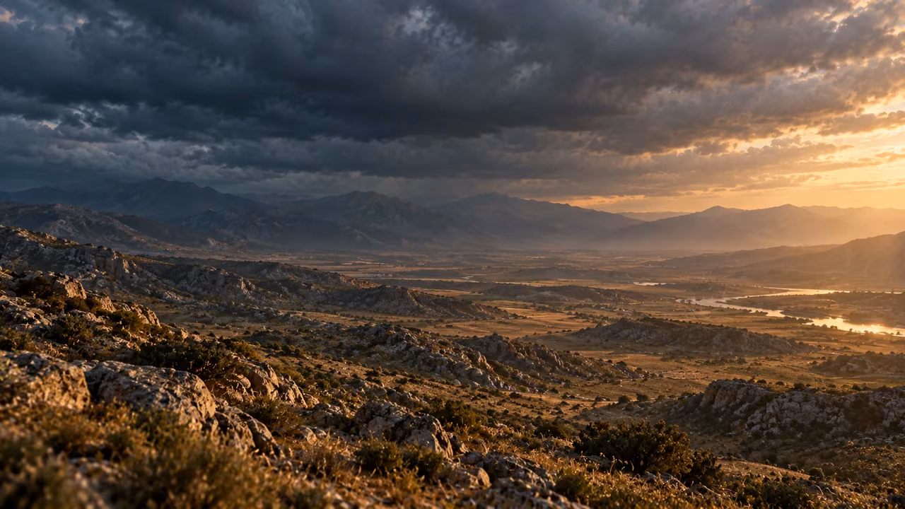 An unoccupied rugged valley lies beneath layered dark cloud and restrained sunlight.