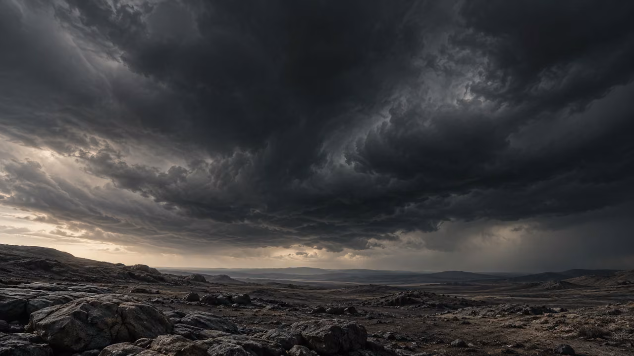 An immense dark cloud expanse hangs over an empty rough landscape.